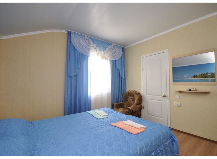 Кровать с лазурным покрывалом, занавесками в тон покрывала, зеркало и кресло в номере «Лагуна» отель Прибой Саки
